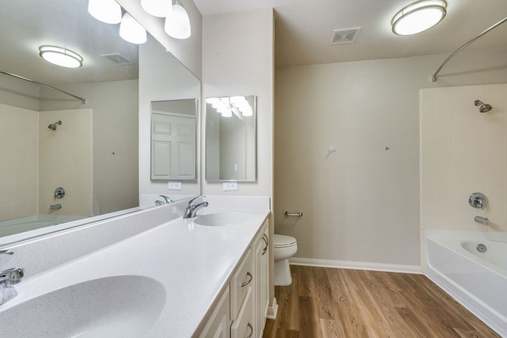 Bathroom with wood flooring, large wall mirror, two sinks, and a bathtub and shower combo with curved curtain rod.