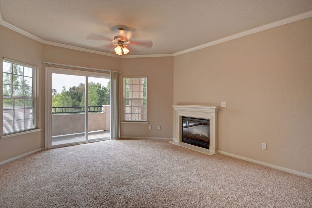 Unfurnished living room with carpet flooring, a ceiling fan, fireplace, and sliding door leading to a balcony.