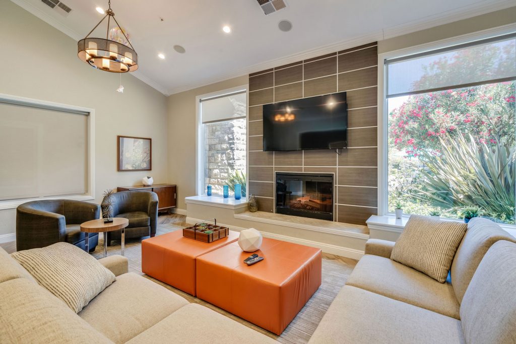 Close up of a lounge area with sectional sofa, chairs, ottoman, and a fireplace with a large wall mounted TV above.
