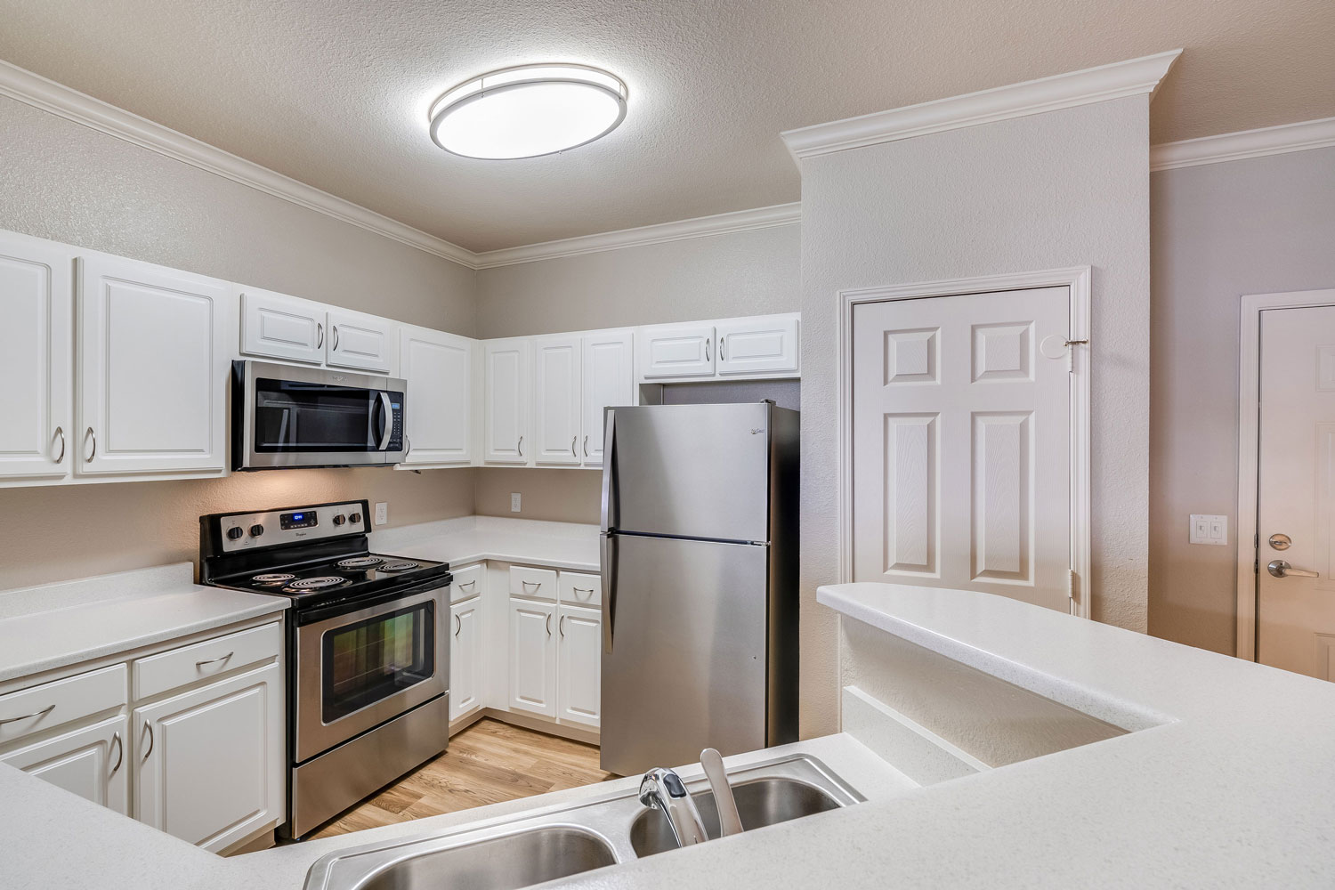 Kitchen with wood flooring, stainless steel appliances, a two-basin sink with a raised bar counter, pantry, and white countertops and cabinets.