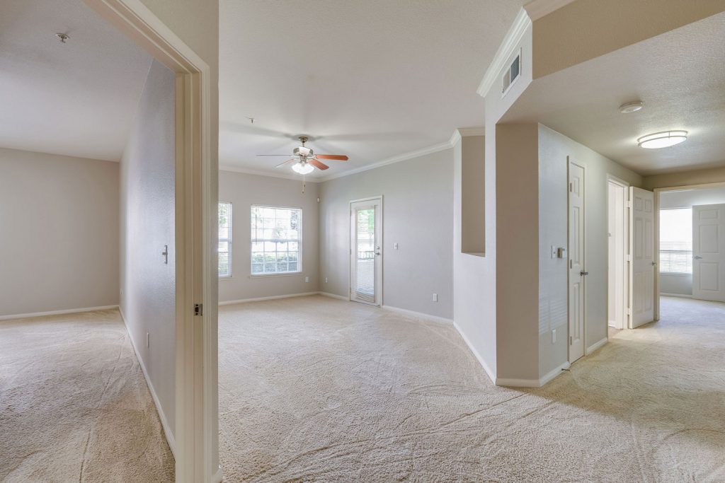Unfurnished living room with carpet flooring, a ceiling fan, patio door, and adjacent hallway and bedroom.
