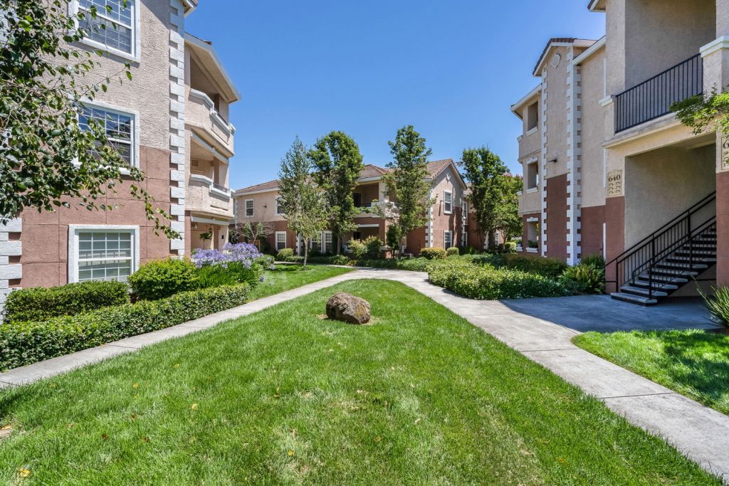 Community courtyard between residential buildings with with lush green landscaping and sidewalks.