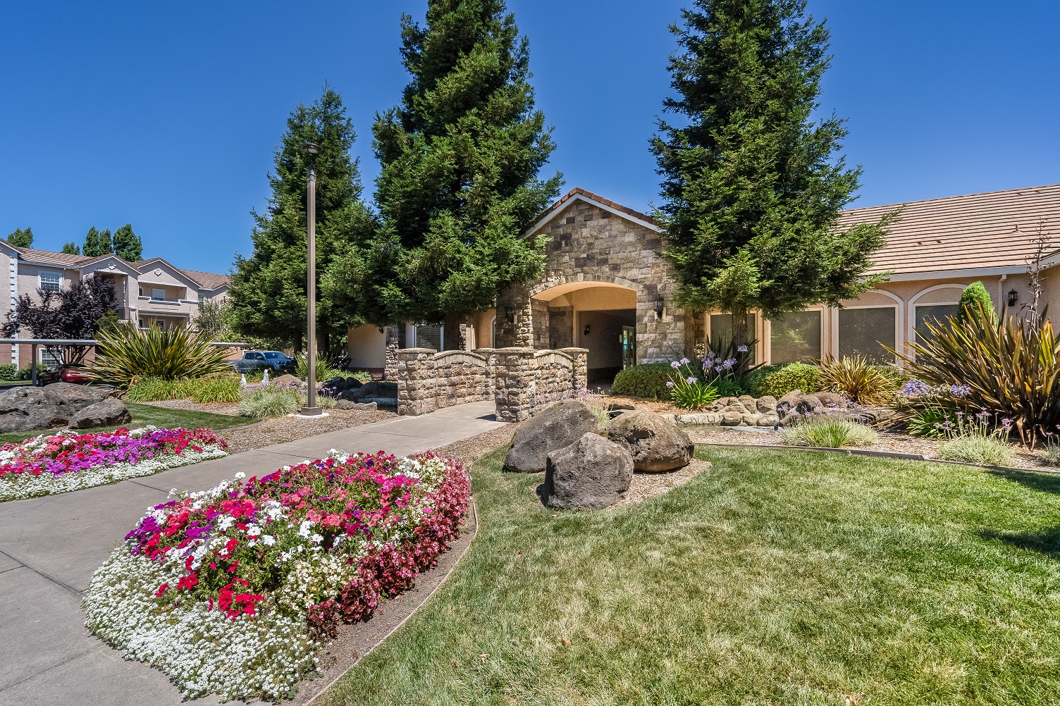 Clubhouse entrance with flowers, green landscaping, and rock feature