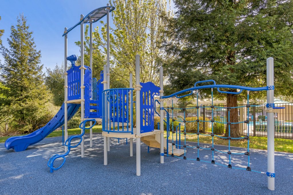 Children’s playground with mulch ground, a surrounding fence, and a covered jungle gym with slide