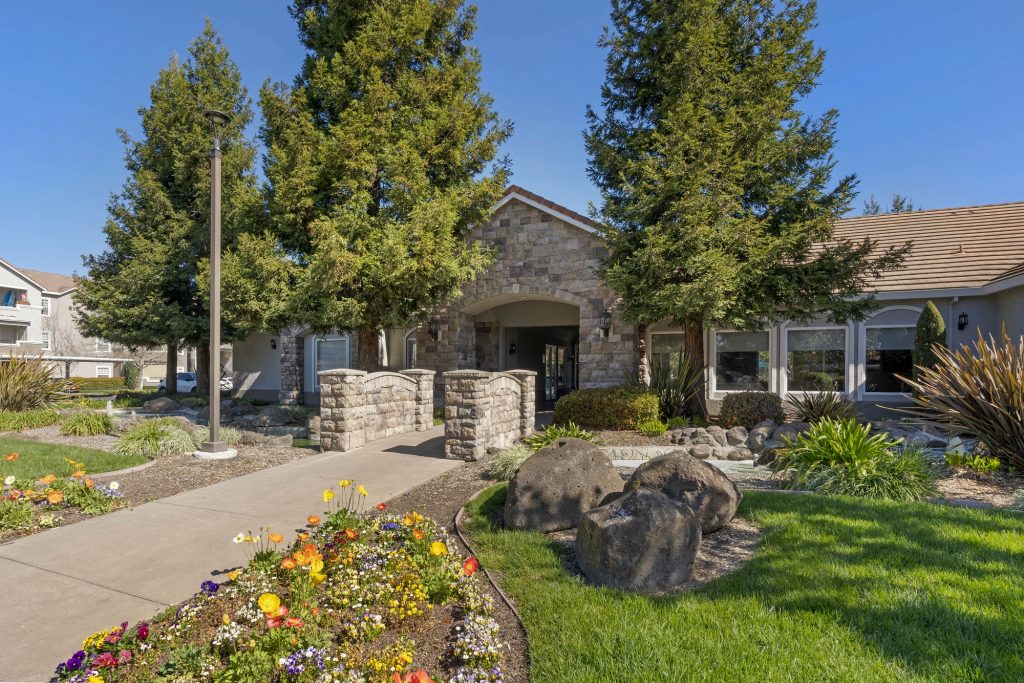Clubhouse entrance with flowers, green landscaping, and rock feature