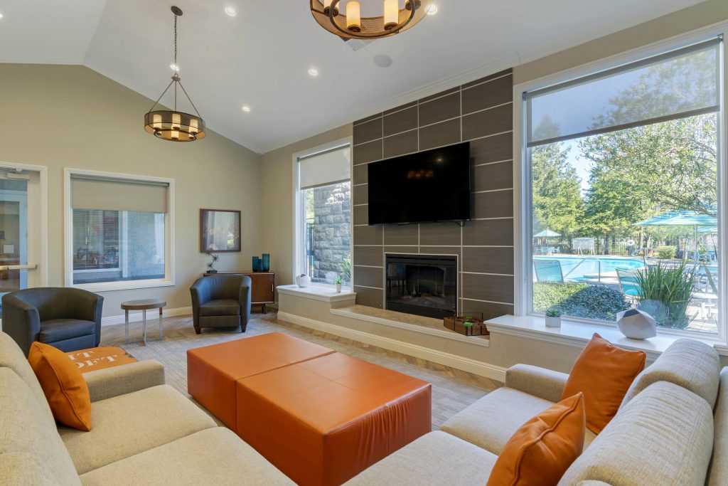 Close up of a lounge area with sectional sofa, chairs, ottoman, and a fireplace with a large wall mounted TV above.