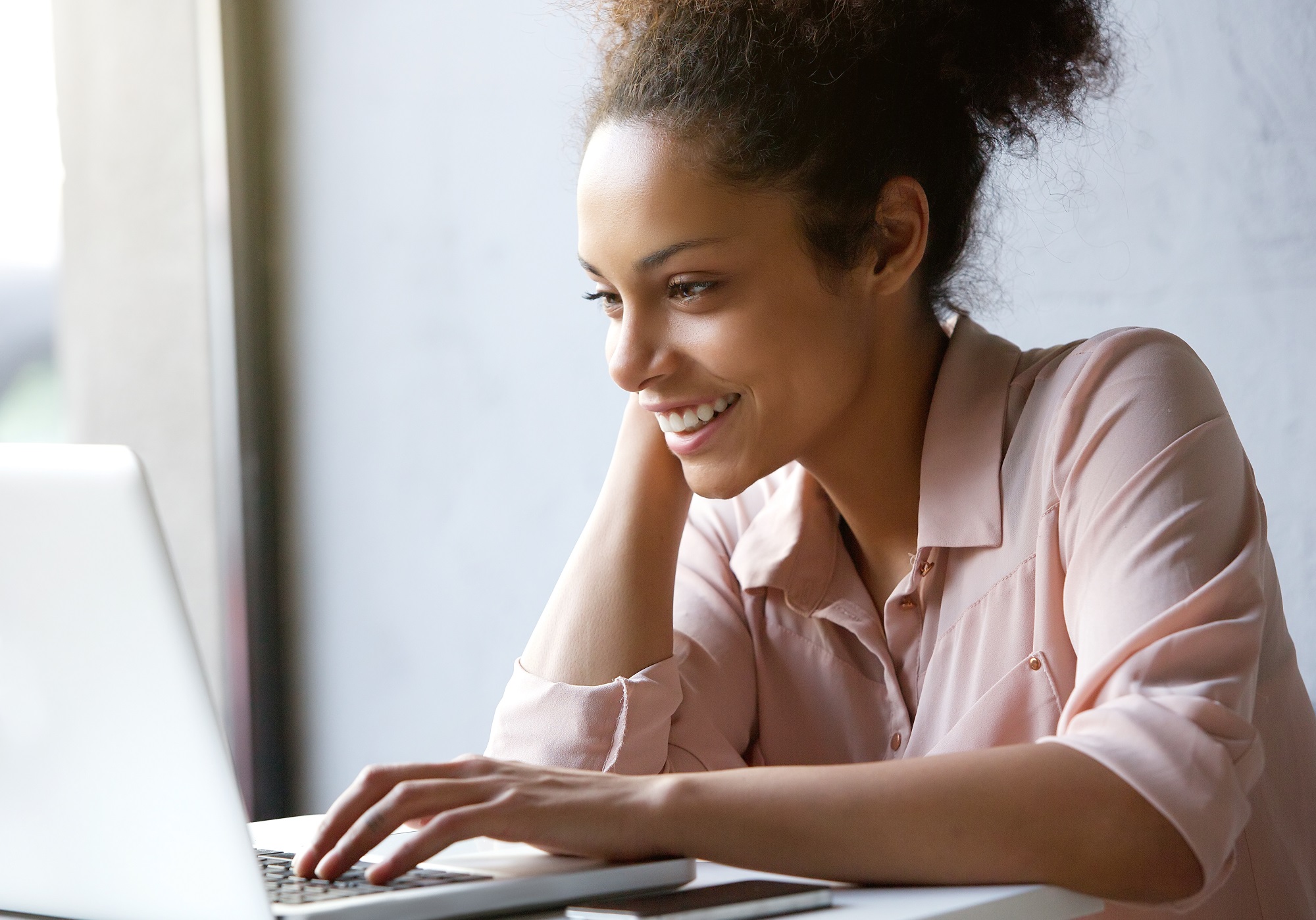 Woman in pink shirt smiling on her laptop at table