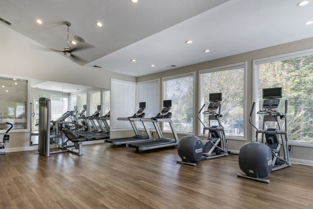 Fitness center with weight machines, benches, free weights, medicine balls, yoga ball, and a mirror wall.